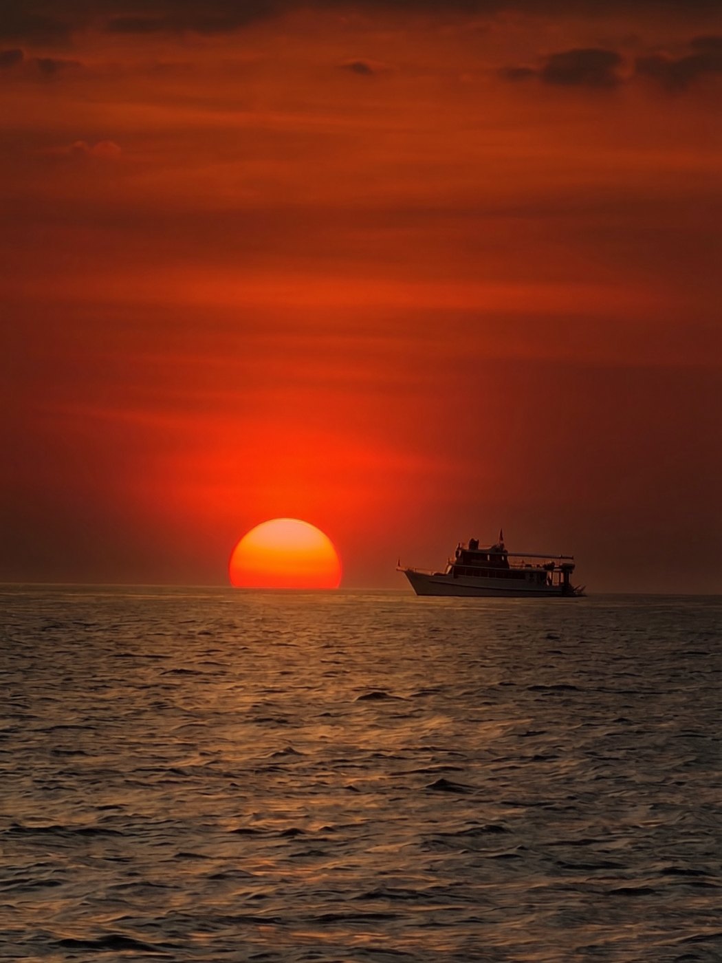 A red sun setting over the sea near Phuket, with a boat on the horizon